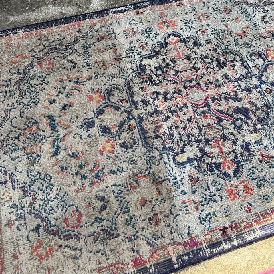 An area rug half cleaned, vivid navy and coral where Mark has cleaned and dull grey where he hasn't yet