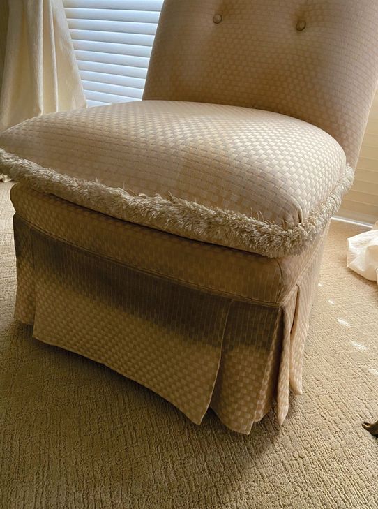 Cream upholstered slipper chair with dark soiling along the skirt from a puppy