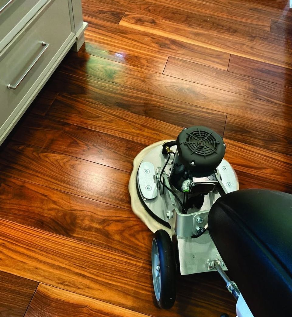 Mark's floor machine with a white cleaning pad on a glossy walnut hardwood floor beside kitchen cabinets